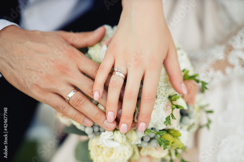 The bride and groom in wedding suits are holding together a wedding bouquet of white and lilac roses. Men's blue classic suit for men and girls white dress. Newlyweds without faces