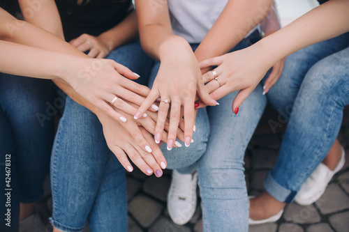 Young girls girlfriends in white T-shirts and jeans folded their arms at each other and show manicure and rings. Team building women in nature. Bachelorette party