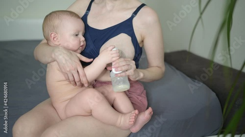 Young mother with newborn cute infant naked baby boy, holding him on arms, using breast pump hugging and breastfeeds with breast milk. Healthy child, concept of hospital and happy motherhood. Nursery