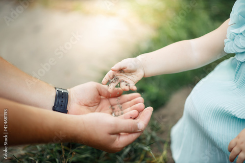Little girl child in a blue dress pours hands on his hands to his father a handful of black earth. The child’s hands hold the earth and give it to dad. Close up without faces only hands
