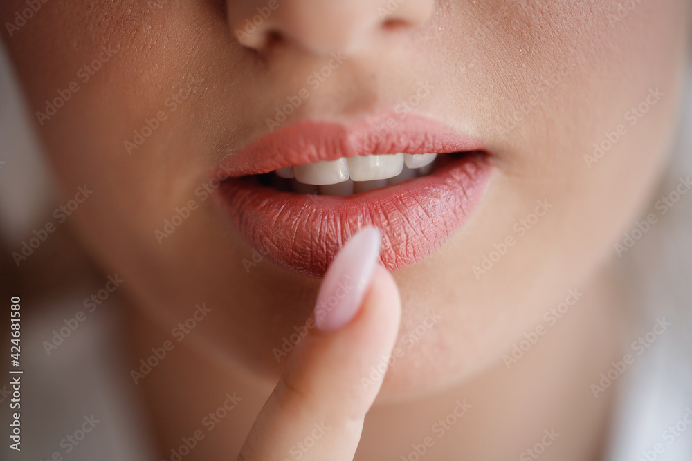Obraz premium The bride girl with large magnificent lips and healthy white teeth presses a finger with a long manicure to her mouth. Very close-up, macro shot
