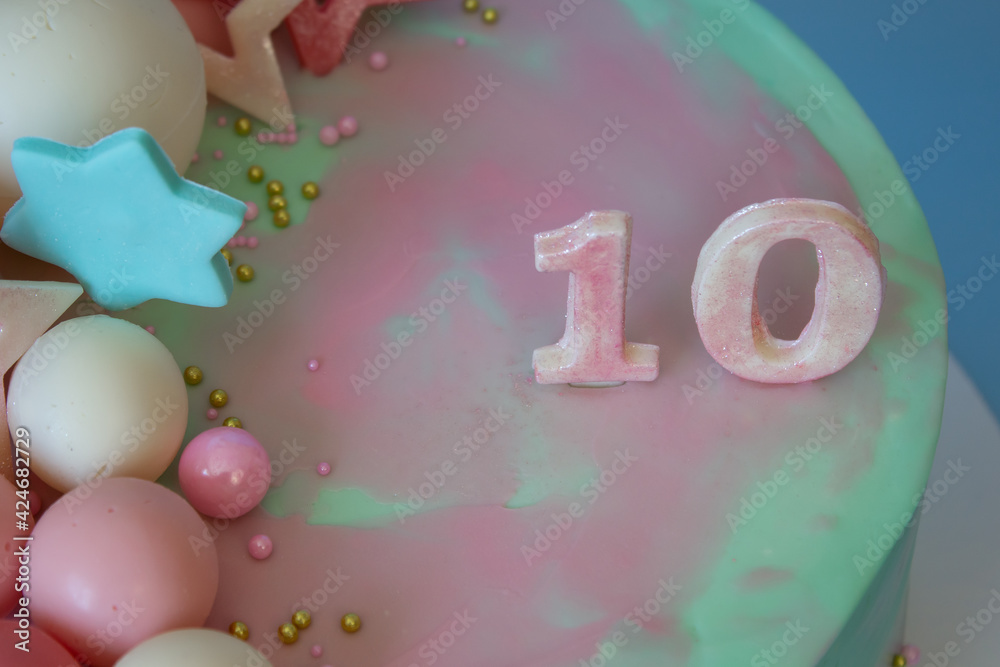 A beautiful birthday cake decorated with chocolate balls and pink and blue stars. With number 10 on a blue background. Place for an inscription.