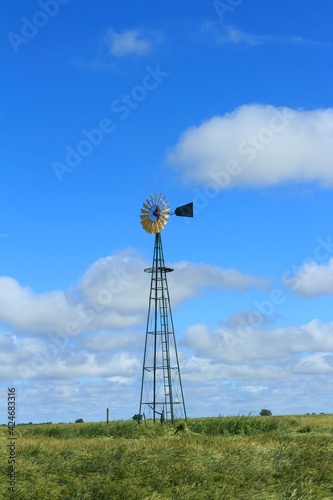 Kansas Windmill in a green Wheat field with blue sky and white clouds north of Lyons Kansas USA out in the country.