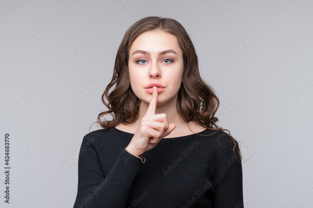 Beautiful serious young woman holding finger at her lips, saying Shh, Hush, demanding keeping secret and holding tongue Beautiful serious young woman holding finger at her lips, saying Shh, Hush, demanding keeping secret and holding tongue