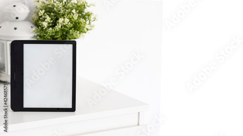 E-book on white book shelf with green plant. Modern reader device mocke up large background Copy space