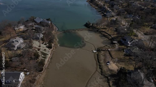 Pan down reveal of a harbor inlet at low tide, adjacent to and fed by Hingham Harbor, separated by a stone wall. Drone. Cove. photo