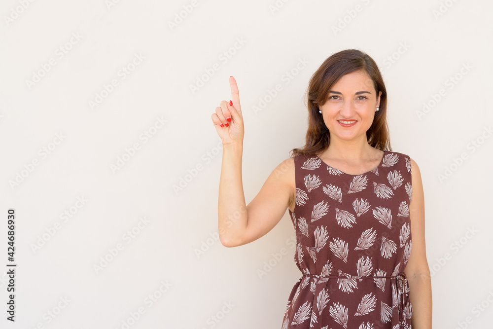 Portrait of beautiful woman pointing finger to copy space outdoors againt plain wall Portrait of beautiful woman pointing finger to copy space outdoors againt plain wall