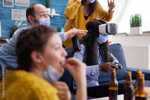 African woman experiencing virtual reality playing video games with vr headset and joystick in home living room while friends are cheering up for her keeping social distancing because of global