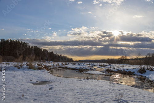 Sun through the clouds. Snow is melting. Early spring. Radiation of the river. Sun rays. Spring landscape