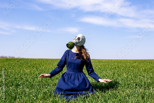 A young girl in a gas mask stands in a green field. Pandemic. Coronavirus.