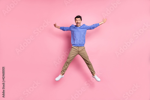 Full size photo of brunet optimistic guy jump wear blue shirt pants sneakers isolated on pink color background