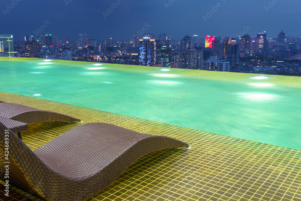 Fototapeta premium Relaxing chairs on Infinity pool with Hanoi skyline on background