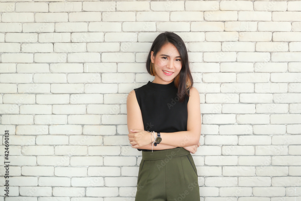 Portrait of young and cute Asian woman standing against white brick wall crossed arms in self-confident pose and smile with friendly and happy face. Portrait of young and cute Asian woman standing against white brick wall crossed arms in self-confident pose and smile with friendly and happy face.