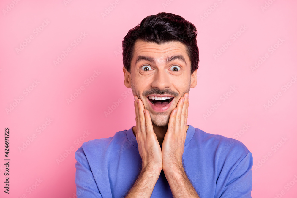 Photo of amazed shocked charming young man hold hands cheekbones isolated on pastel pink color background Photo of amazed shocked charming young man hold hands cheekbones isolated on pastel pink color background