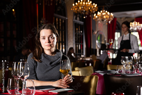 Young woman holding glass of white wine in luxurious restaurant