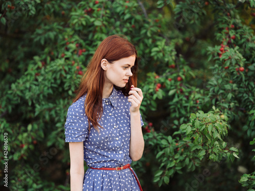 Portrait of a romantic woman in a blue dress near green bushes with red berries