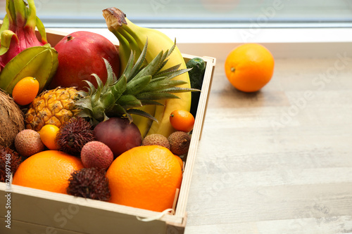 Assortment of exotic fruits in wooden crate on floor, closeup. Space for text