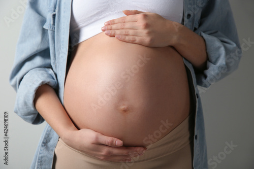 Pregnant woman touching her belly on light grey background, closeup