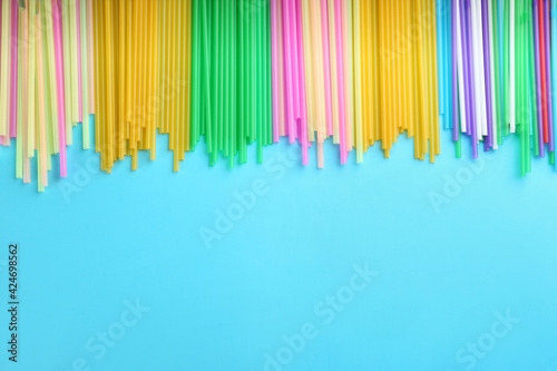 Colorful plastic drinking straws on light blue background  flat lay. Space for text