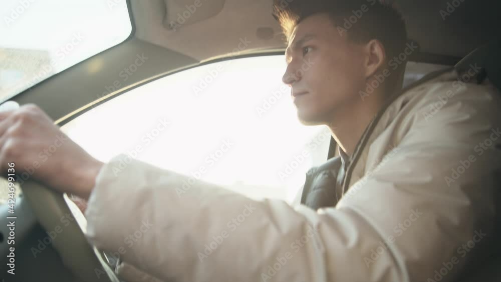 A young Asian guy in a light jacket, drives a car. A man driving a car. City driving with a right-hand drive. A young driver is mastering city driving skills. sunny day A young Asian guy in a light jacket, drives a car. A man driving a car. City driving with a right-hand drive. A young driver is mastering city driving skills. sunny day