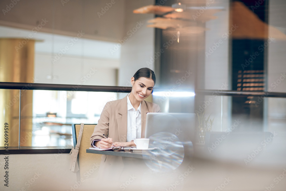 Young businesswoman in beige jacket sitting in the office in front of the laptop