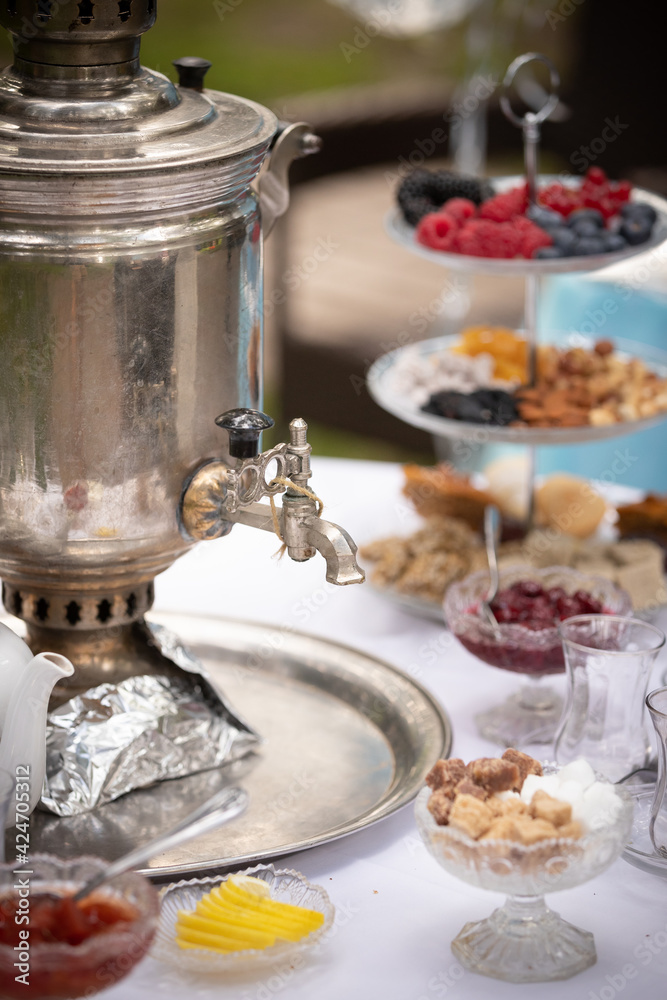 View of a round table with tea-ware from a traditional Russian samovar. Bakery, sweet food concept. Delicious pastries, jam and berries on the table. Birthday celebration. Children's holiday.