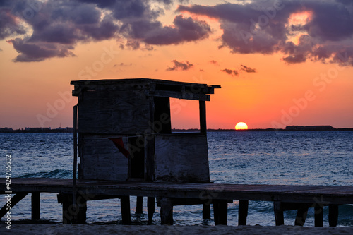 caseta de madera en la playa al atardecer con el sol poniendose el en horizonte photo