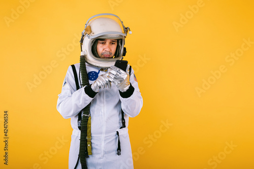 Fototapet Male cosmonaut in space suit and helmet, talking on the mobile phone, on yellow background