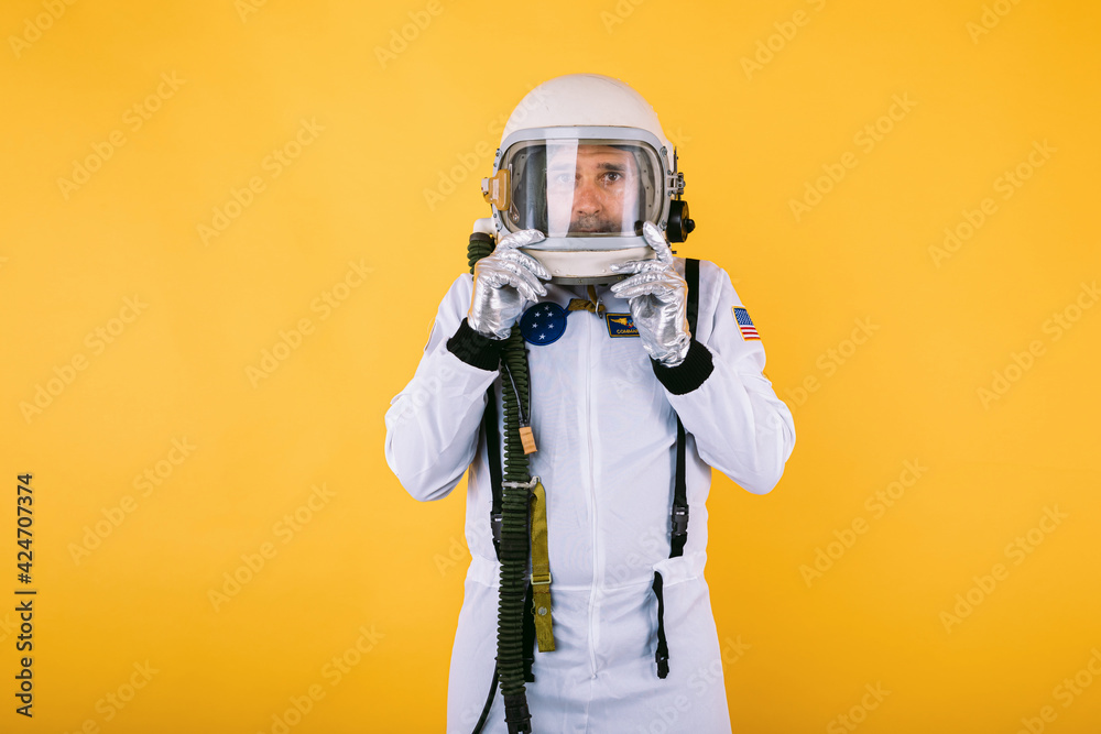 Male cosmonaut in space suit and helmet, holding helmet with misted glass, on yellow background. Male cosmonaut in space suit and helmet, holding helmet with misted glass, on yellow background.
