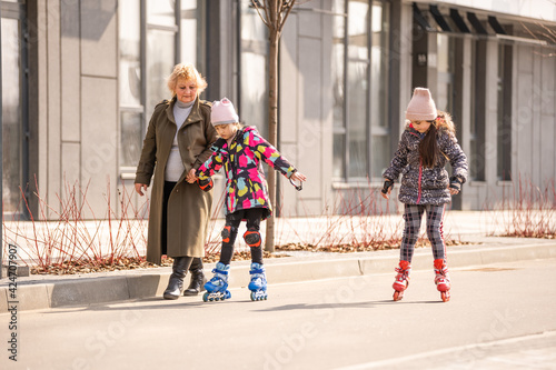 A happy family in roller skates, grandma teaches two granddaughters to roller-skate