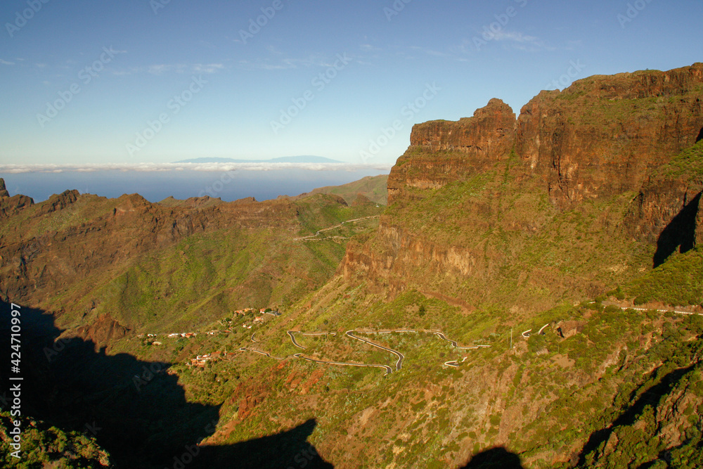 La carretera con curvas que desciende al barranco de Masca (cañón), isla de Tenerife, Islas Canarias, España. Isla de La Palma en el horizonte rodeada de nubes en el océnao Atlántico.