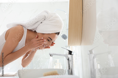 Happy young woman washing face in bathroom