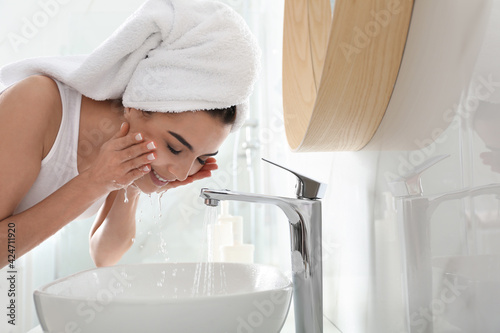 Happy young woman washing face in bathroom photo