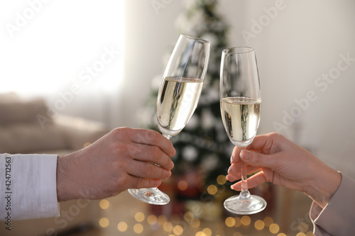 Εκτύπωση καμβά Couple clinking glasses of champagne in room decorated for Christmas, closeup