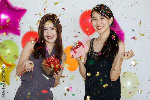 Delighted Asian girlfriends standing under confetti