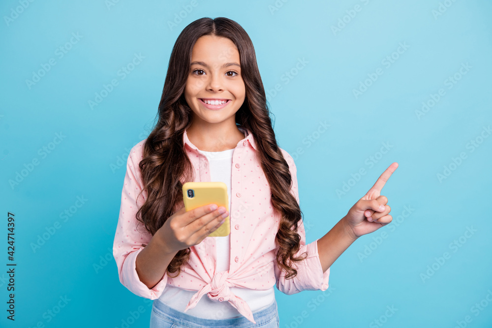 Portrait of wavy hairdo beautiful pupil direct finger empty space toothy smile isolated on blue color background Portrait of wavy hairdo beautiful pupil direct finger empty space toothy smile isolated on blue color background