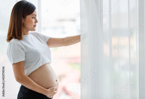 Free Download Asian woman pregnant mother standing near window in white bedroom - GFXLoad