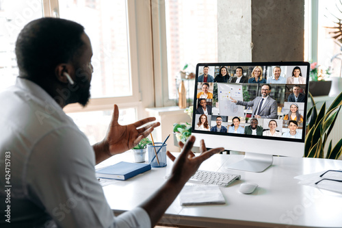 African American successful man, ceo, manager, consultant, holding an online business conference, with multiracial employees, sitting at their desk at home, gesturing hands, discuss about strategy