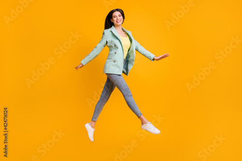Full size photo of young attractive lovely pretty smiling girl jumping wear green blazer isolated on yellow color background