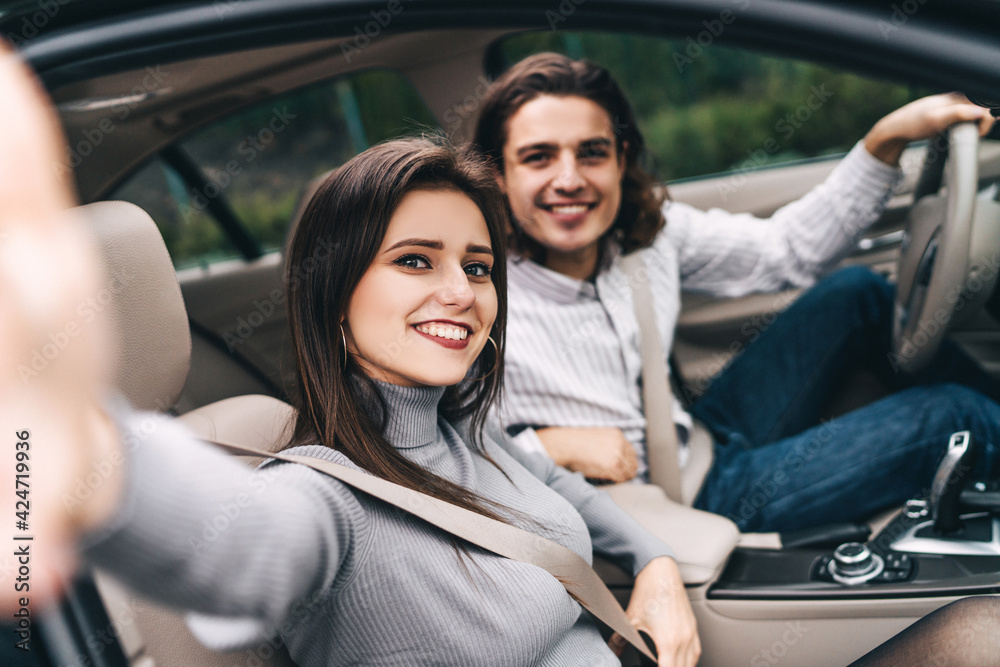 Happy young couple in the car, enjoying the trip, taking a selfie for memory, good impressions of a modern car