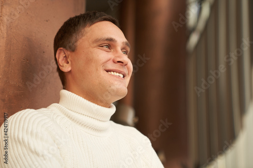 The handsome man in the room smiles and looks into the distance. A man in a white sweater. Copy space. High quality photo