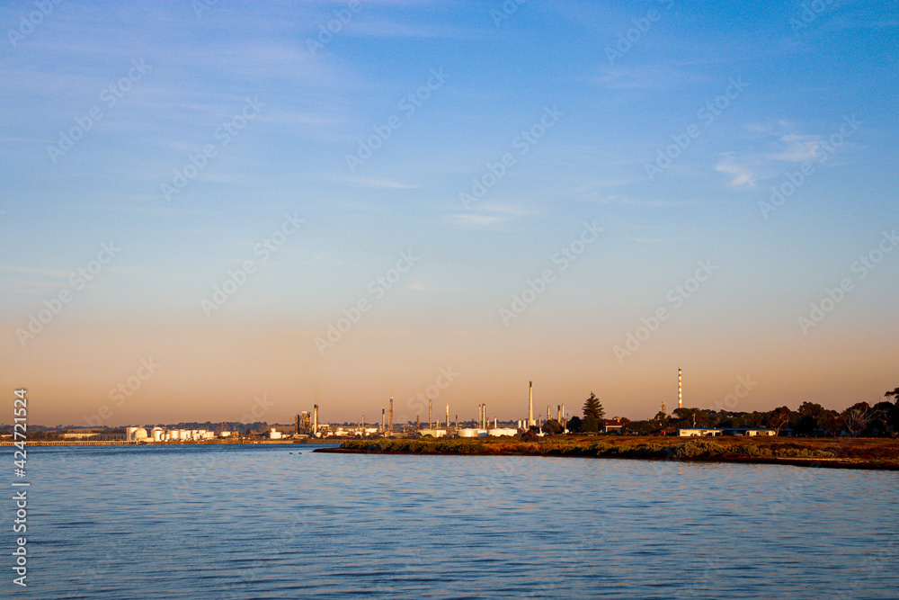sunrise over the sea with industrial facilities and refineries in the distance
