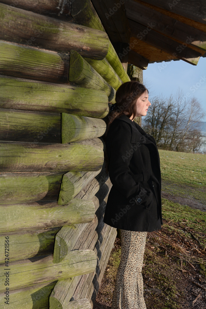Fototapeta premium Young girl leans against a wooden hut