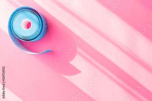 Blue roll of kinesiology tape on pink background with trendy sun light and shadows and copy space, flat lay. Recovery, anti-aging procedures. Kinesio taping