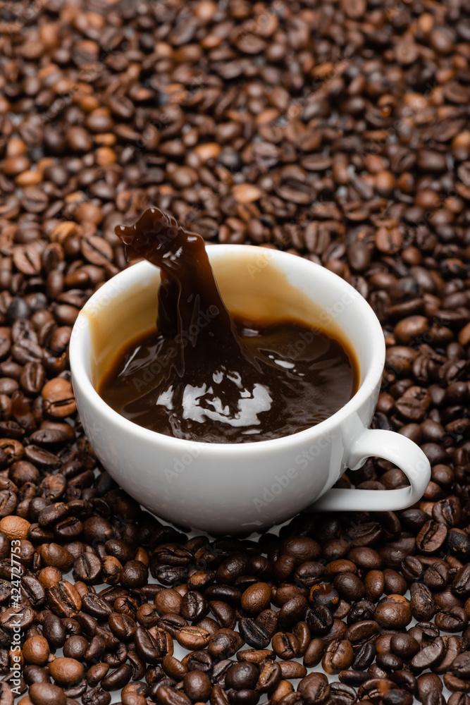 Fototapeta premium white cup with prepared coffee splashing on brown beans