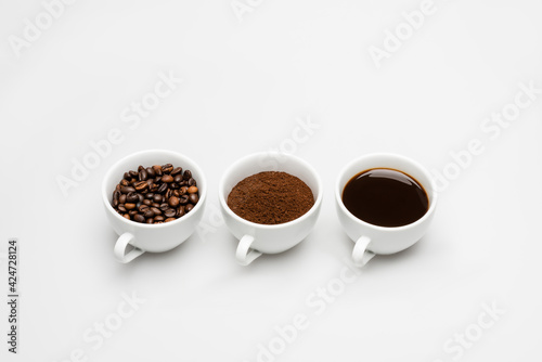 cups with ground and prepared coffee near beans on white