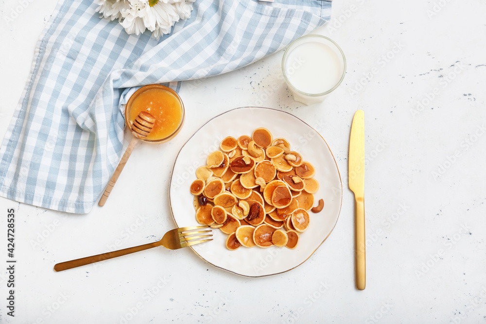 Plate with tasty mini pancakes, honey and milk on white background Plate with tasty mini pancakes, honey and milk on white background