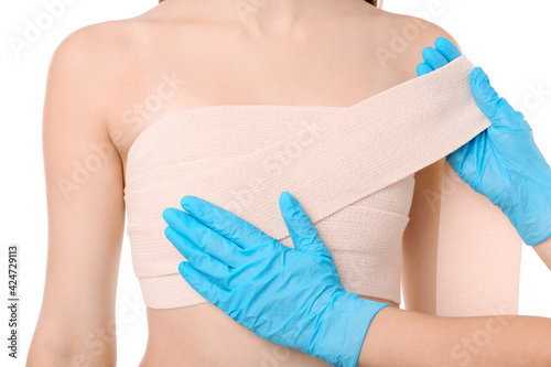 Doctor applying bandage on female chest after cosmetic surgery operation against white background