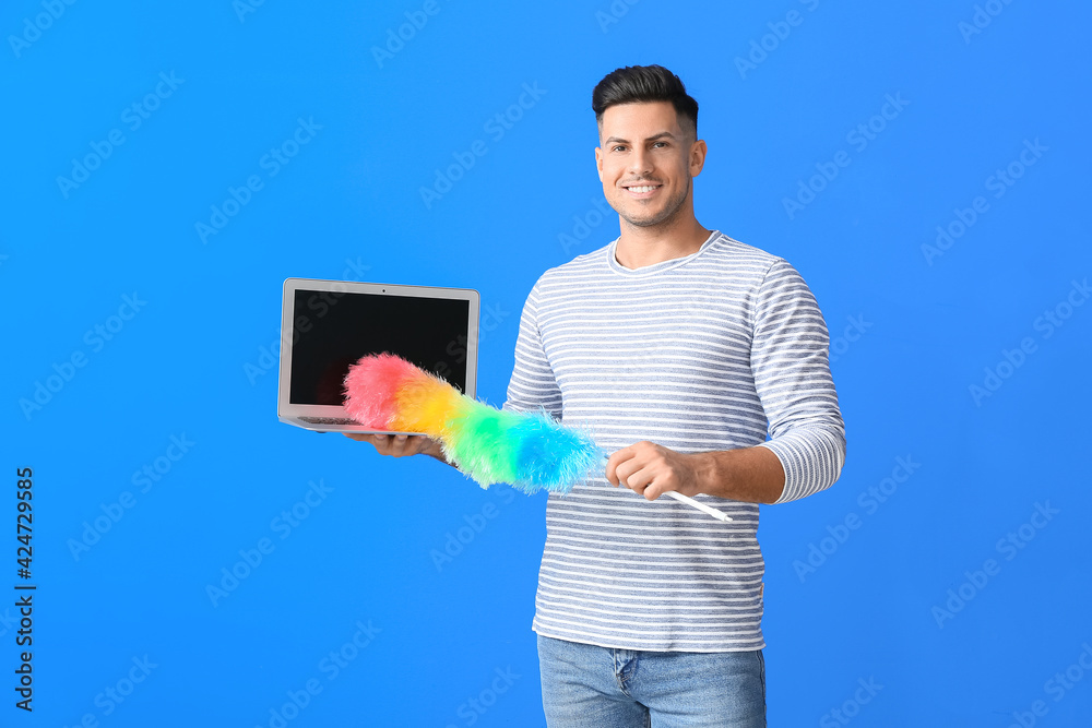 Young man with laptop and dust brush on color background Young man with laptop and dust brush on color background