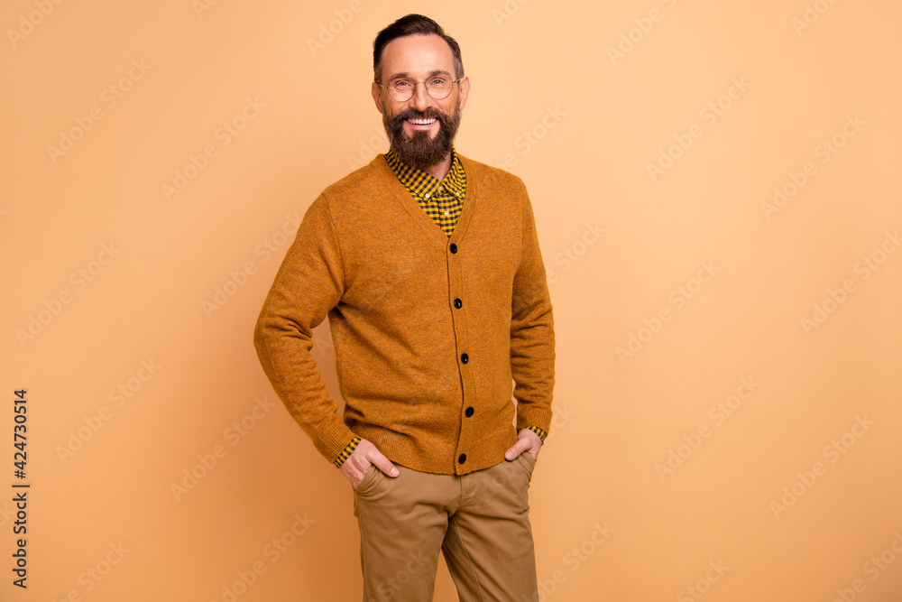 Photo of optimistic brown hair man stand wear spectacles brown sweater isolated on beige color background Photo of optimistic brown hair man stand wear spectacles brown sweater isolated on beige color background
